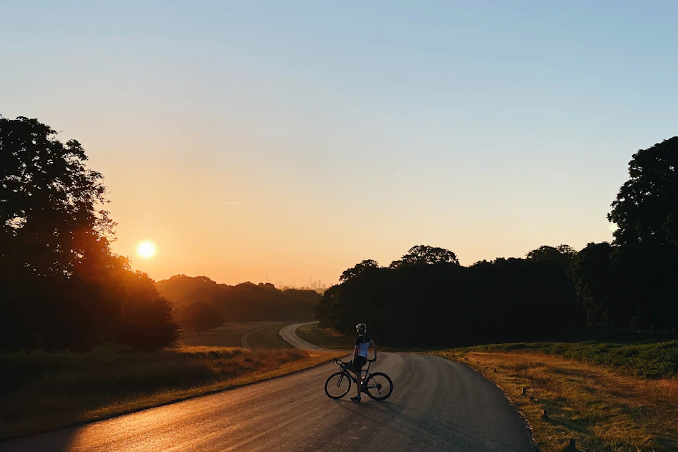 A lone cyclist on a tree-lined road in Richmond Park at sunrise