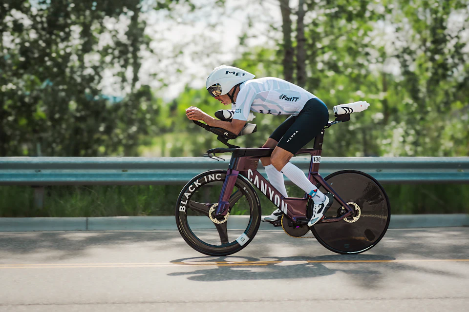 A triathlete riding an aerodynamic time trial bike on a road