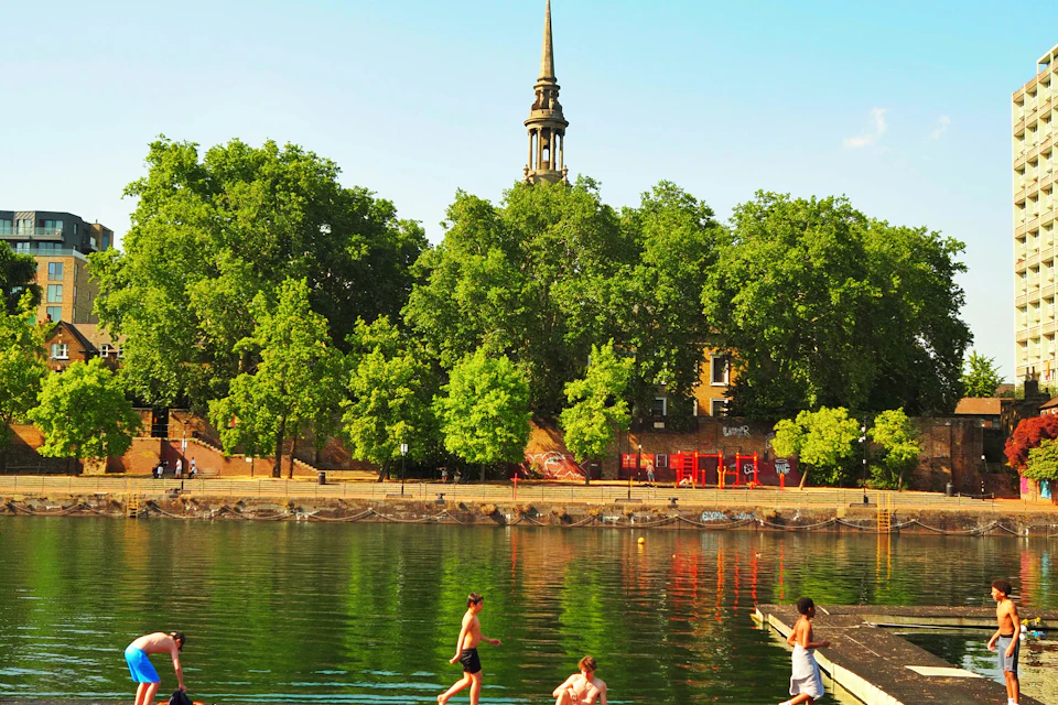 People swimming and sunbathing from a wooden dock at a London lake
