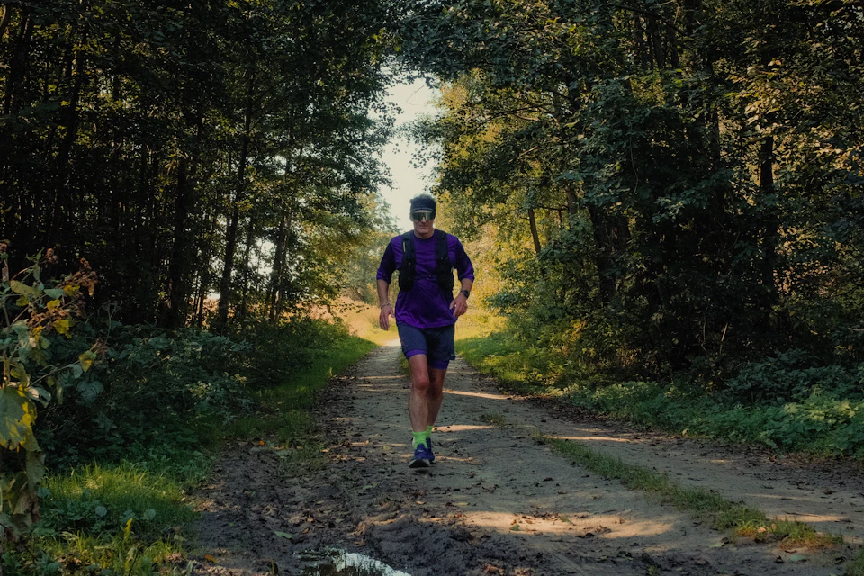 A man running along a dirt path through a sunlit wood