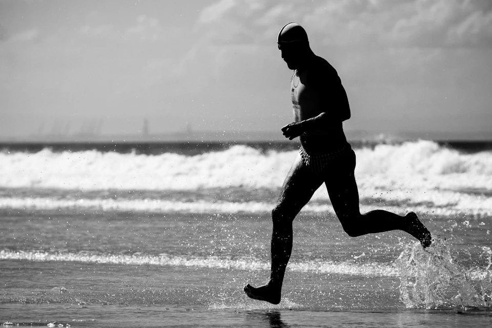 A triathlete in a one-piece suit running out of the surf, seen in silhouette