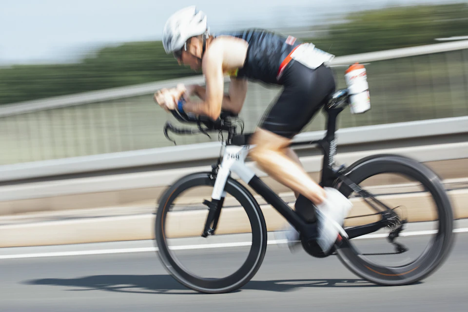 A triathlete in black on a white bike riding on a road