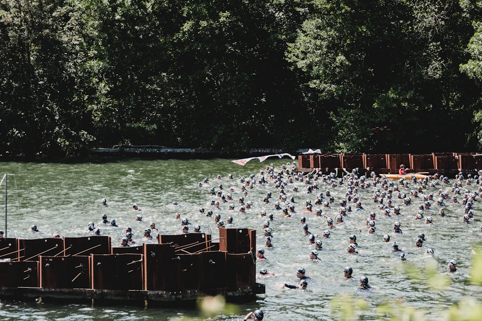 A large crowd of swimmers gathered in a lake beside a pontoon at a mass swim start