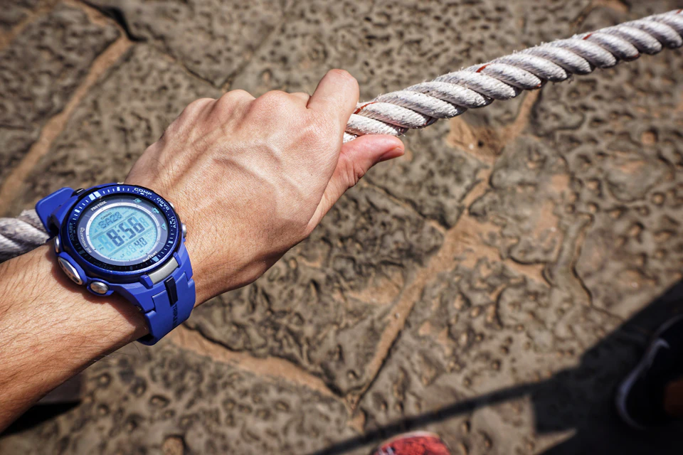 A blue digital sports watch on a wrist gripping a rope