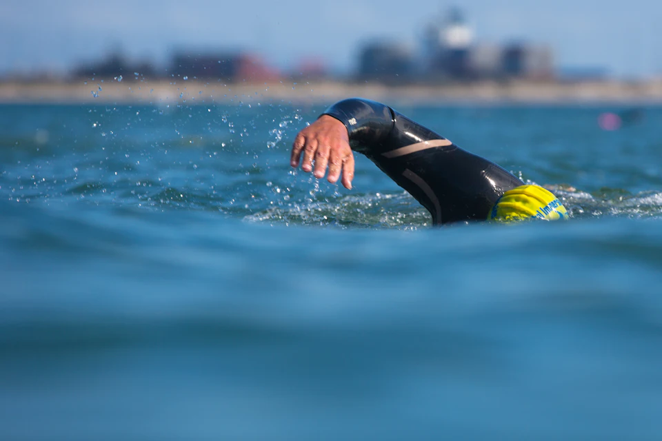 A swimmer in a black wetsuit mid-stroke in open water